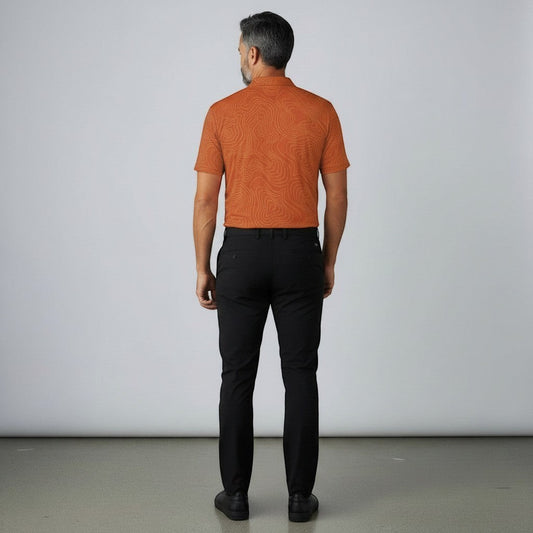 Rear view of a man wearing a BREAKPOINT Sportswear burnt orange performance polo with a topographic print and black trousers