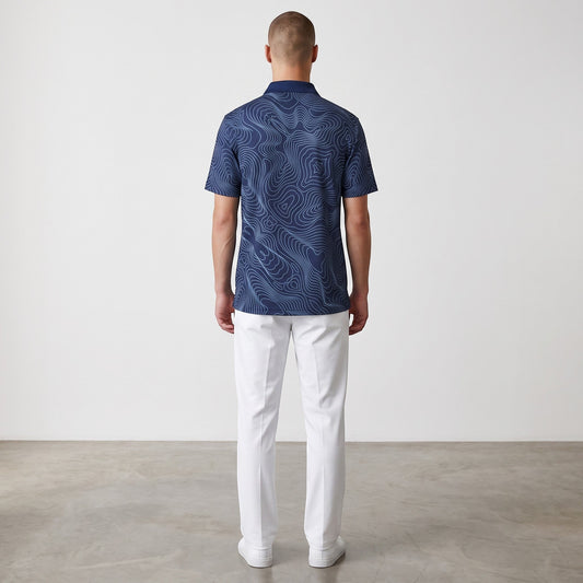Back view of a man wearing a BREAKPOINT Sportswear navy performance polo with a topographic print and white trousers.