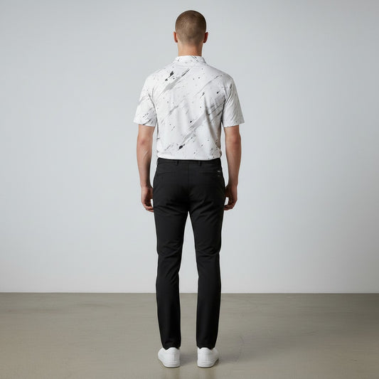 Rear view of a man wearing a BREAKPOINT Sportswear white performance polo with a black splatter print and black trousers