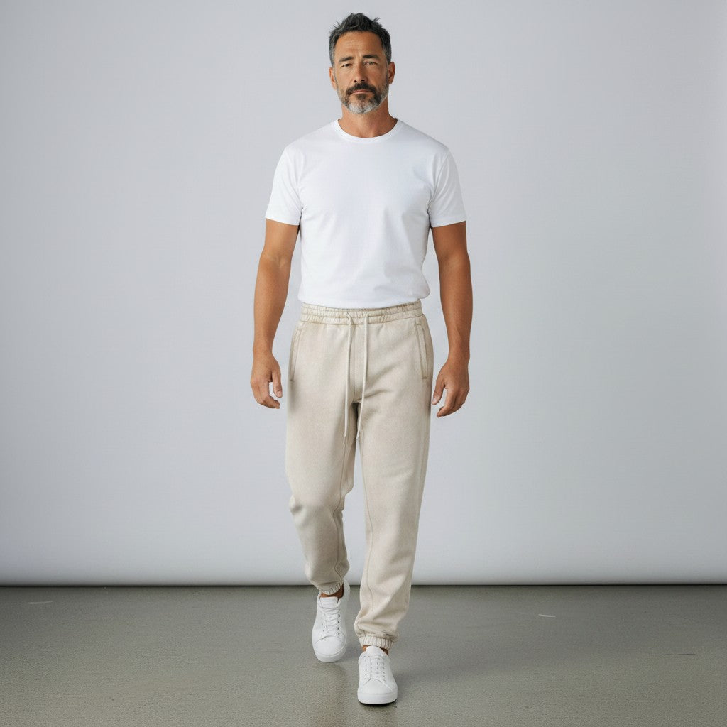 A man wearing BREAKPOINT Sportswear beige fleece sweatpants with a white t-shirt and sneakers in a studio setting.
