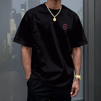 BREAKPOINT Sportswear unisex black drop-shoulder t-shirt with a small pink logo on the chest, worn by a man.