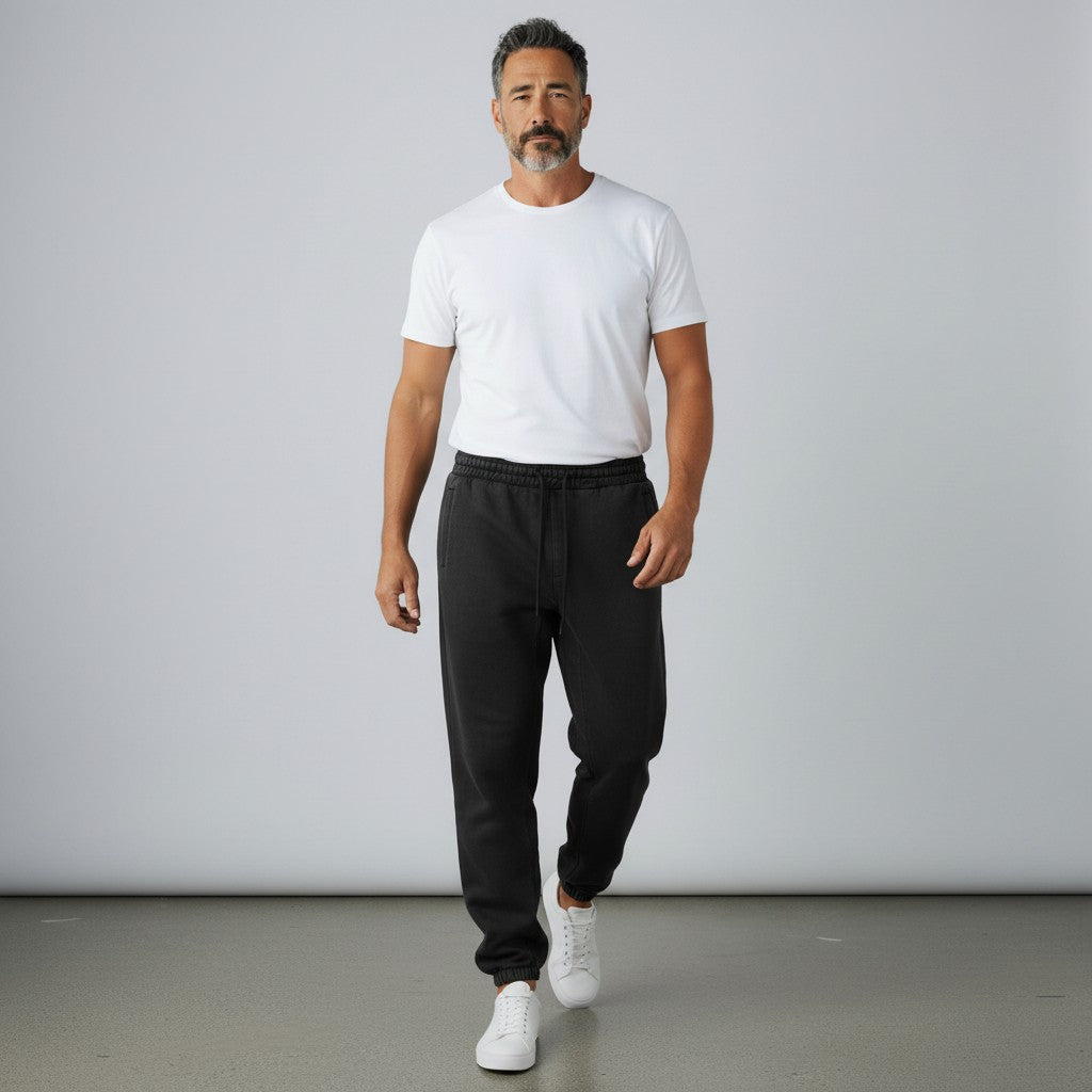 Man wearing BREAKPOINT Sportswear black fleece sweatpants with a white t-shirt and sneakers in a studio setting