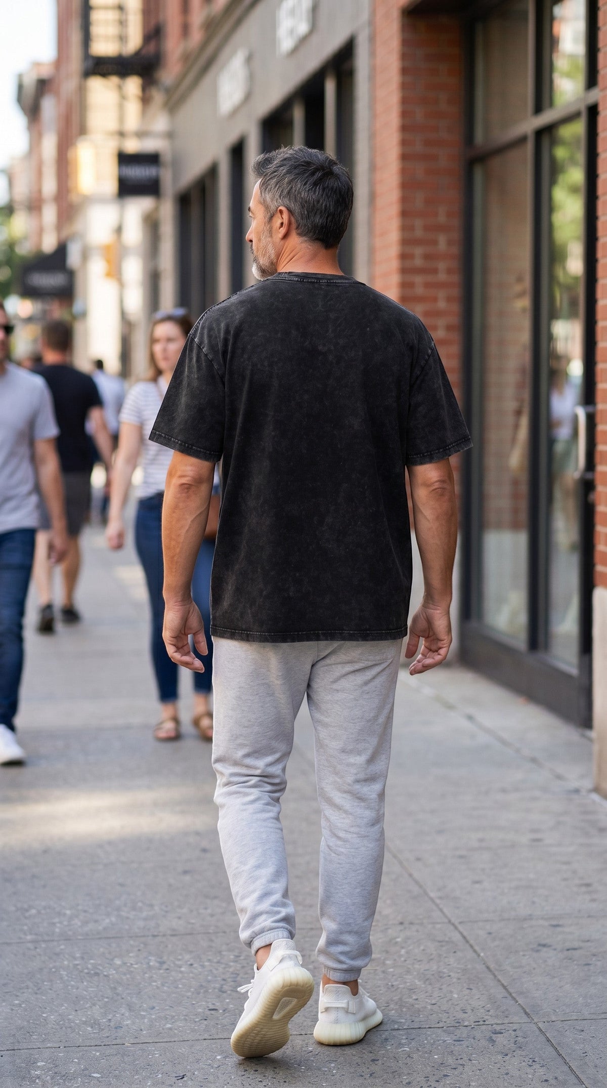 A man wearing a BREAKPOINT Sportswear black snow wash cotton t-shirt with a drop shoulder fit, walking on a city street.
