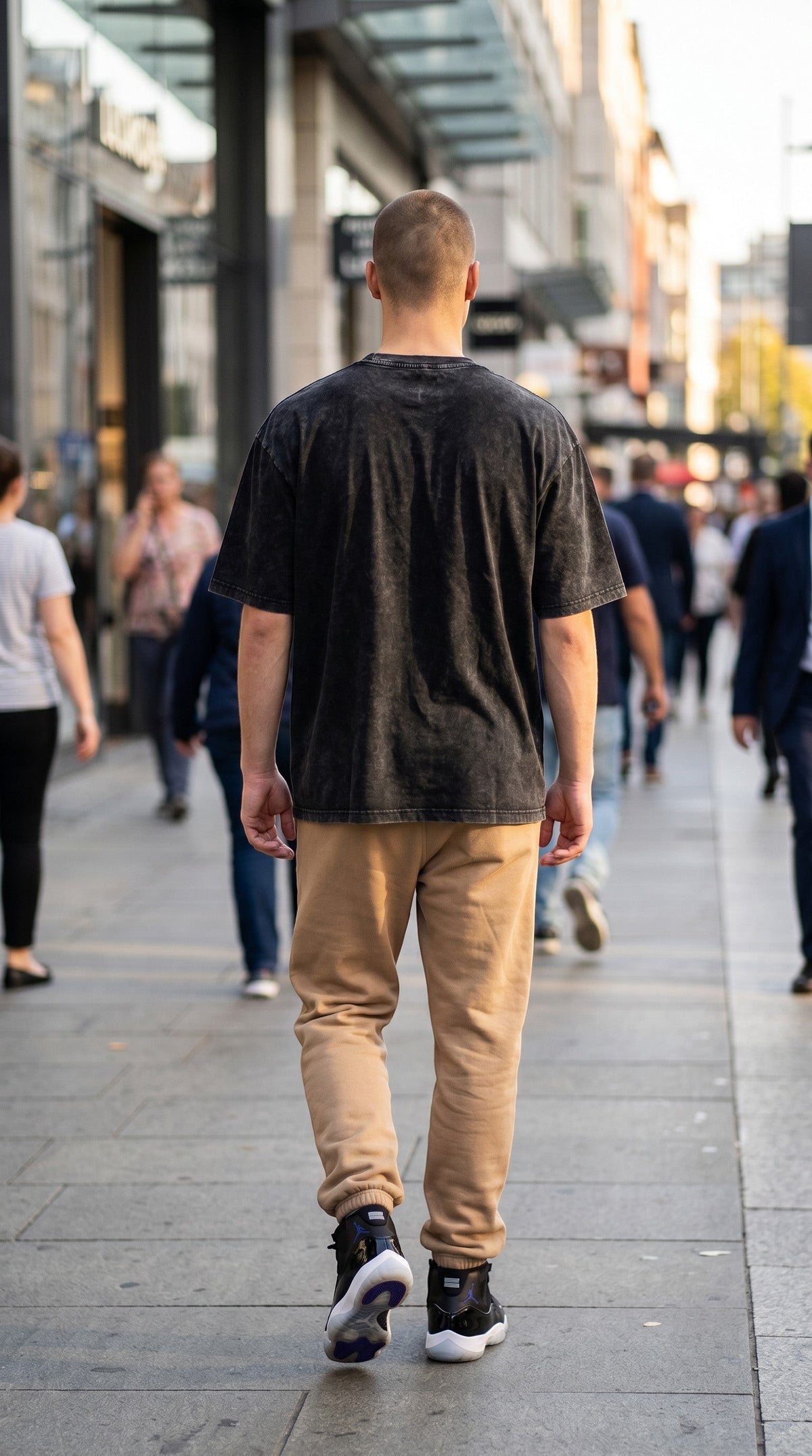 A man wearing a BREAKPOINT Sportswear black snow-washed cotton t-shirt and tan joggers walking on a city street.