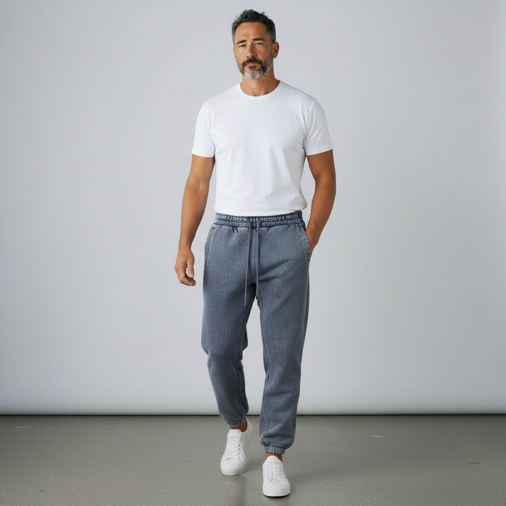 A man wearing BREAKPOINT Sportswear Essential fleece sweatpants in a washed charcoal grey with a white t-shirt and sneakers