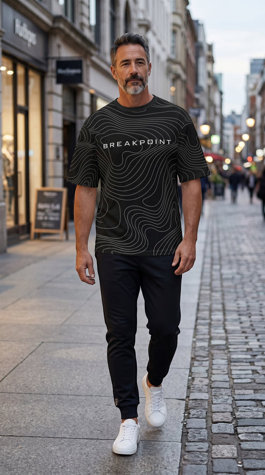 BREAKPOINT Sportswear Courtside Tee in black with white topographic graphic, worn by a man on a city street.