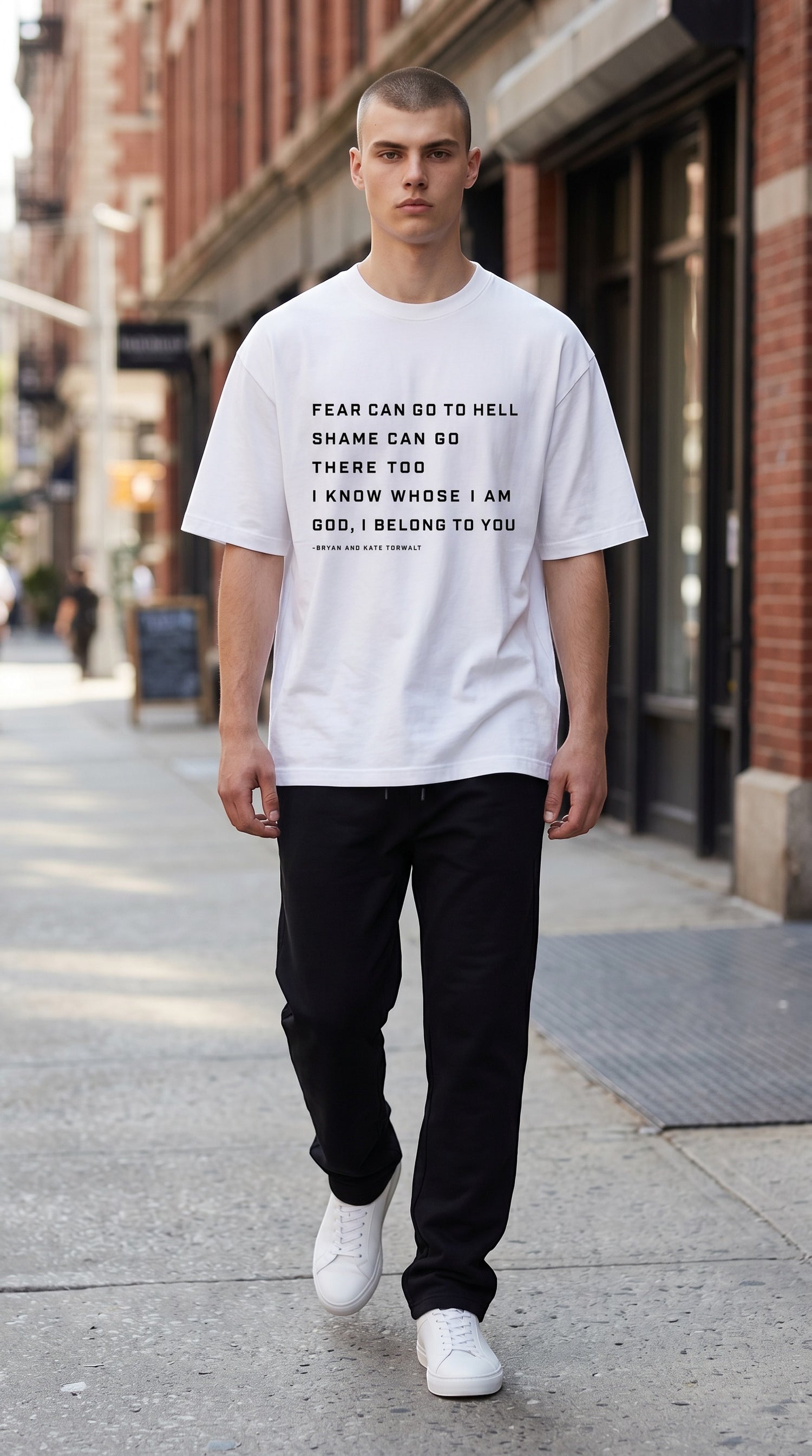 A man wearing a white BREAKPOINT Sportswear Identity Tee with black text, paired with black pants on a city street.