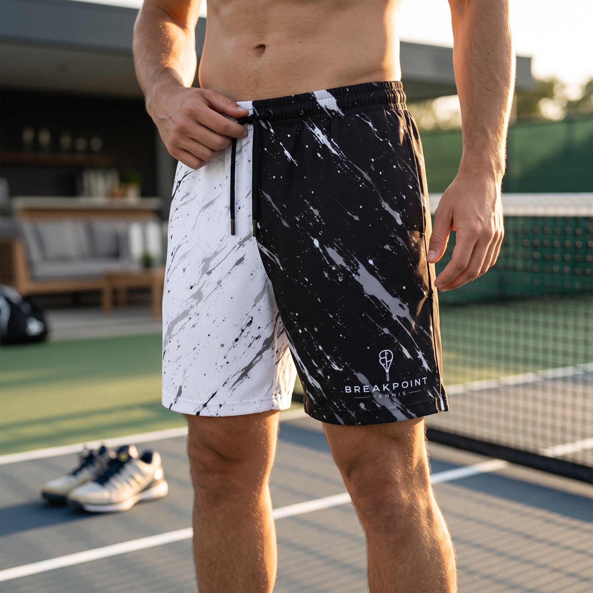 BREAKPOINT Sportswear men's athletic mesh shorts with a black and white paint splatter design on a tennis court.