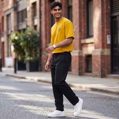 BREAKPOINT Sportswear unisex mustard yellow drop-shoulder t-shirt with logo, worn by a man with black pants and sneakers