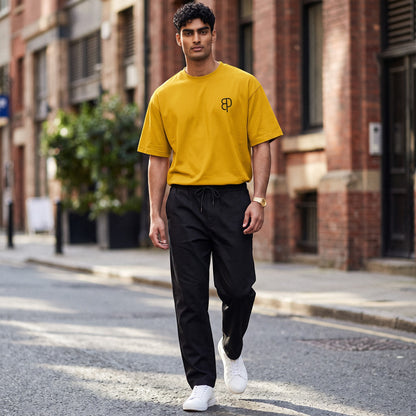 BREAKPOINT Sportswear unisex mustard yellow drop-shoulder t-shirt with black logo, worn by a man on a city street.
