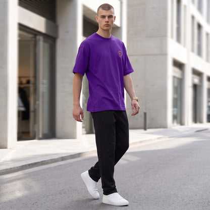 BREAKPOINT Sportswear purple drop-shoulder t-shirt with orange logo on a model walking on a city street.
