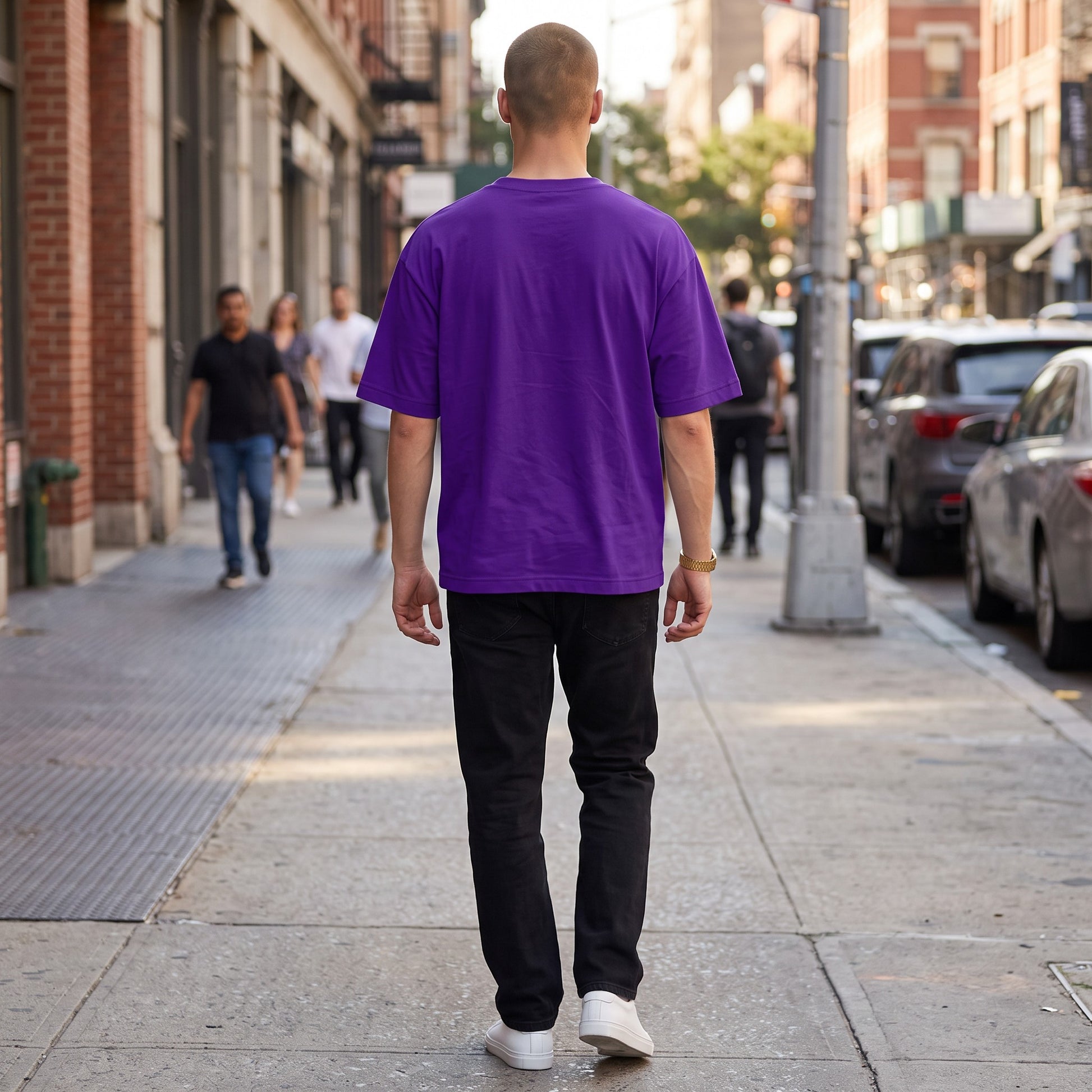 BREAKPOINT Sportswear unisex purple drop-shoulder t-shirt worn by a man walking on a city sidewalk from behind.