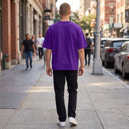 BREAKPOINT Sportswear unisex purple drop-shoulder t-shirt worn by a man walking on a city sidewalk from behind.