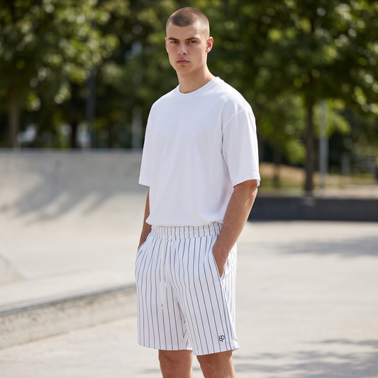 BREAKPOINT Sportswear unisex court shorts in white with black pinstripes, worn by a model in a white t-shirt outdoors.