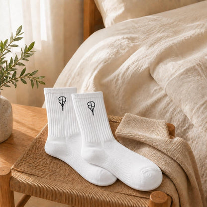 BREAKPOINT Sportswear white cotton crew socks with black embroidered tennis racket logo on a wooden stool