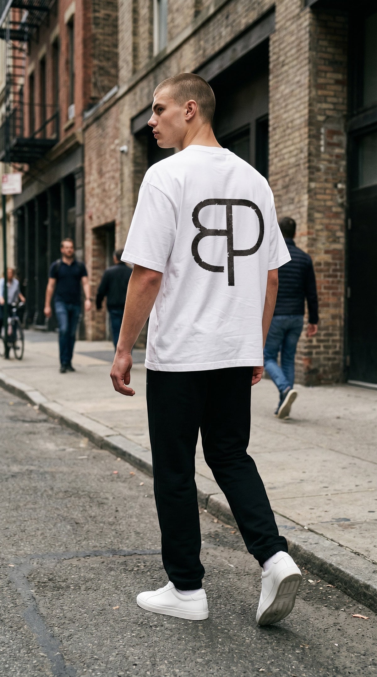 A man wearing a white BREAKPOINT Sportswear cotton tee with a large black logo on the back in an urban street setting.