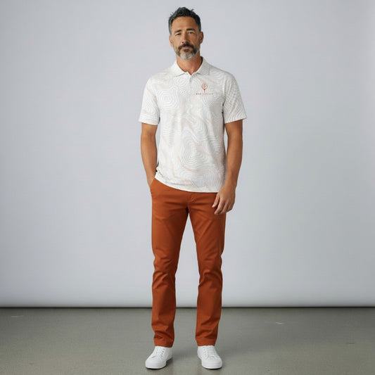 Model wearing a BREAKPOINT Sportswear white performance polo with topographic print and burnt orange trousers.