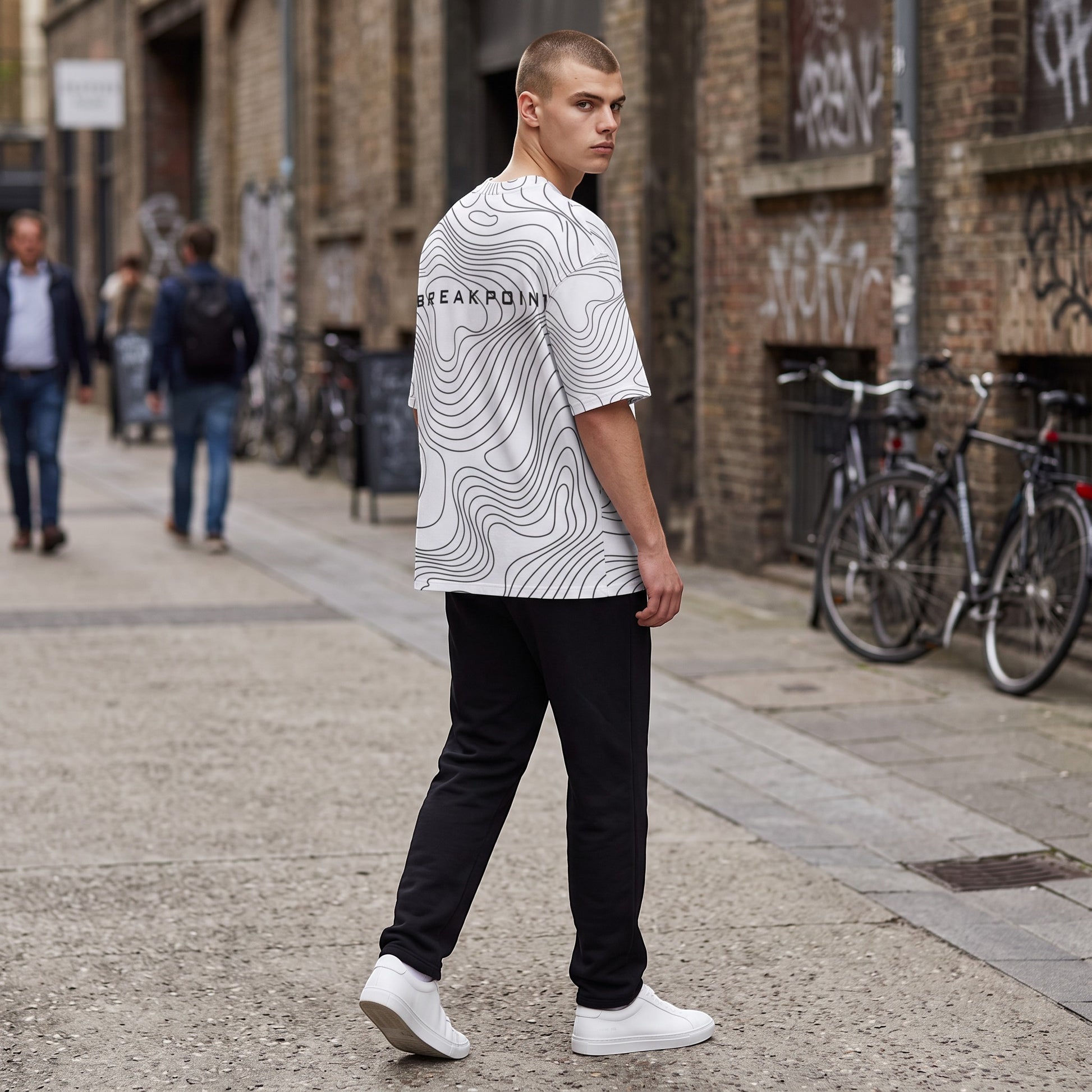 BREAKPOINT Sportswear white drop-shoulder tee with black topographic line print worn by a man in an urban setting.